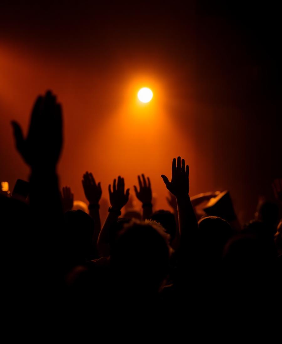 Silhouetted hands raised in worship under warm stage light